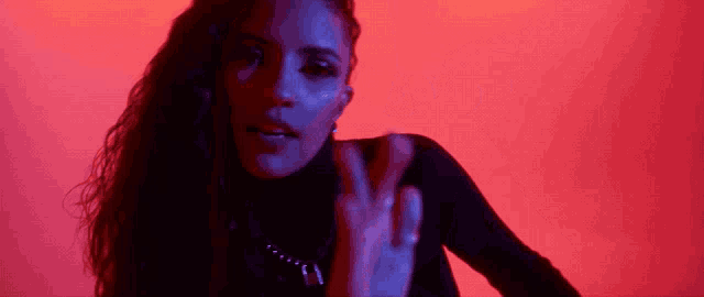 a woman in a black turtleneck is making a peace sign in front of a red background