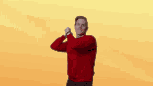 a man in a red sweater is dancing in front of a yellow backdrop