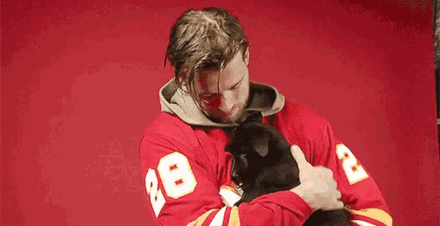 a man in a red jersey with the number 28 on it is holding a black puppy .