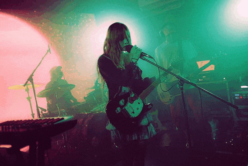 a woman singing into a microphone while playing a guitar in a band