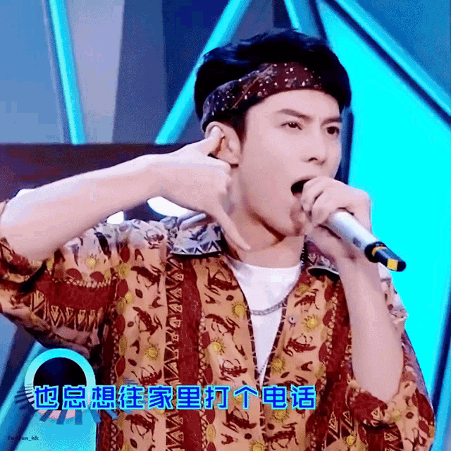 a man wearing a bandana is singing into a microphone with chinese writing behind him