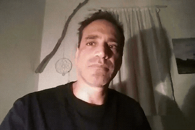 a man in a black shirt stands in front of a wall with a dream catcher on it