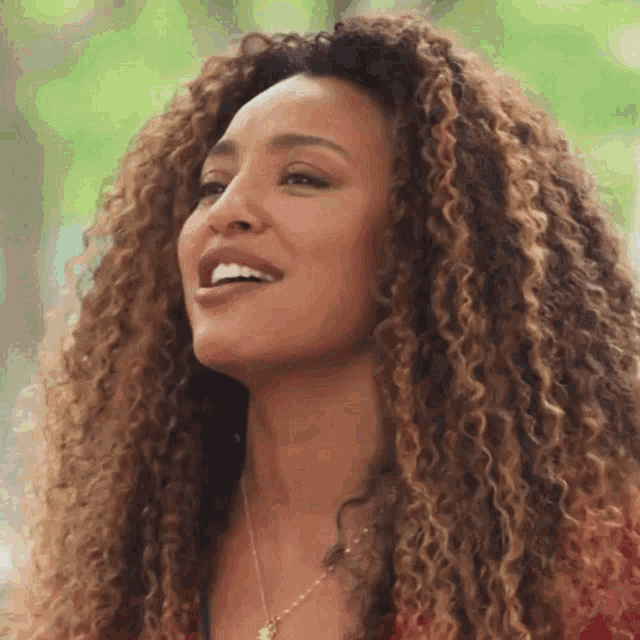 a woman with curly hair is smiling and wearing a red shirt