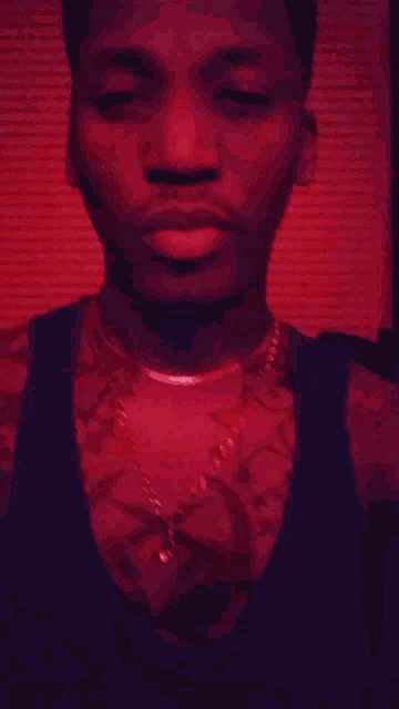a man wearing a necklace and a tank top looks at the camera