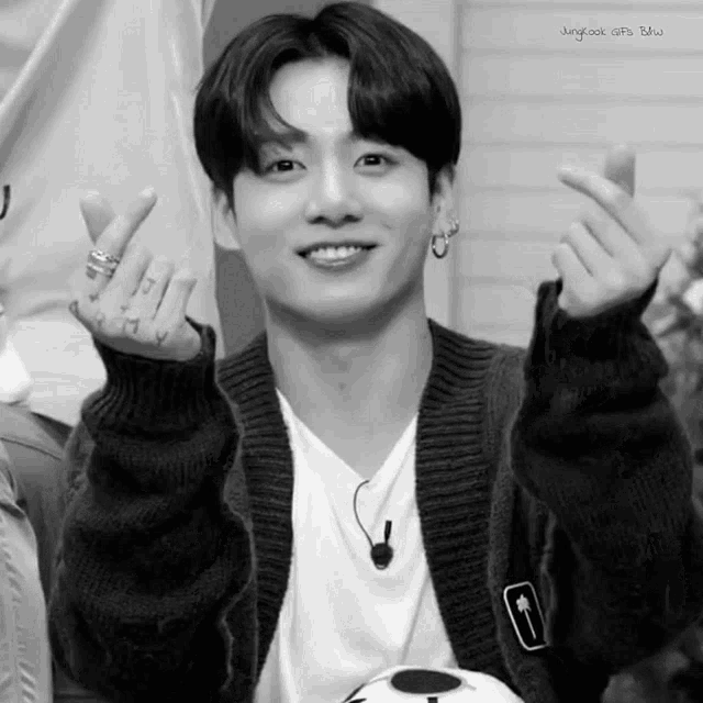 a black and white photo of a young man making a heart shape with his hands .