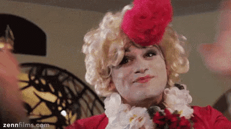 a man in a drag queen costume is wearing a red jacket and a red hat .