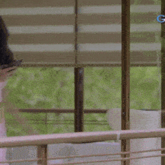 a woman in a white dress is standing in front of a window and looking at her phone .