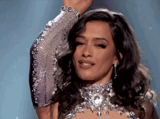 a woman wearing a dress with rhinestones and pearls holds her hand up