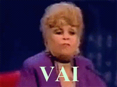 a woman in a purple jacket is making a funny face and the word vai is written on the screen .