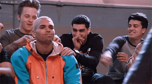 a group of young men are sitting around a man in a colorful jacket who is laughing .