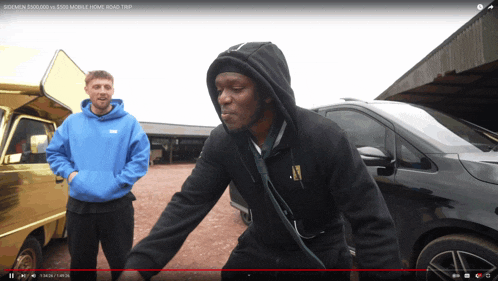a man in a black hoodie is standing in front of a gold van