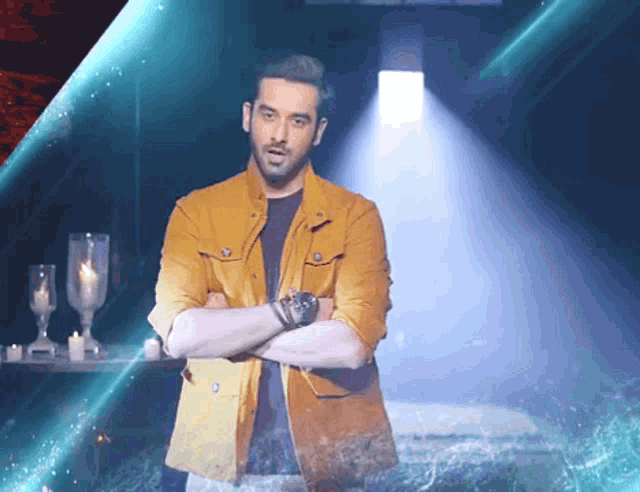 a man in a yellow jacket stands with his arms crossed in front of candles