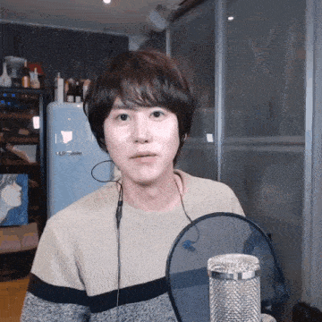 a young man wearing headphones and a sweater stands in front of a microphone