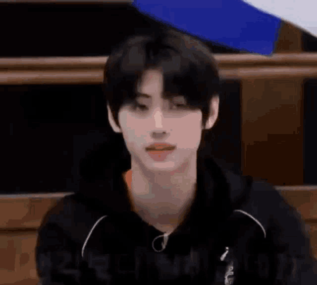 a young man in a black hoodie is making a funny face while sitting in front of a microphone .