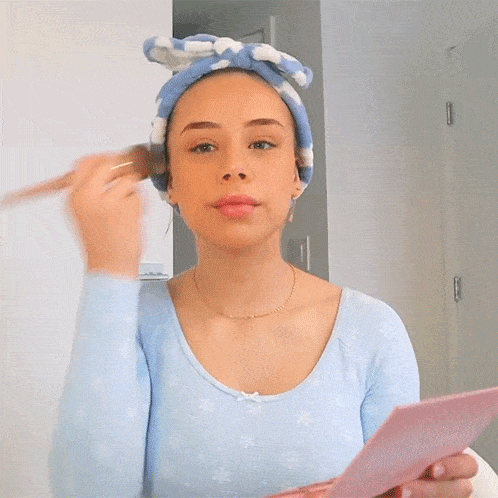 a woman wearing a headband applying makeup with a brush