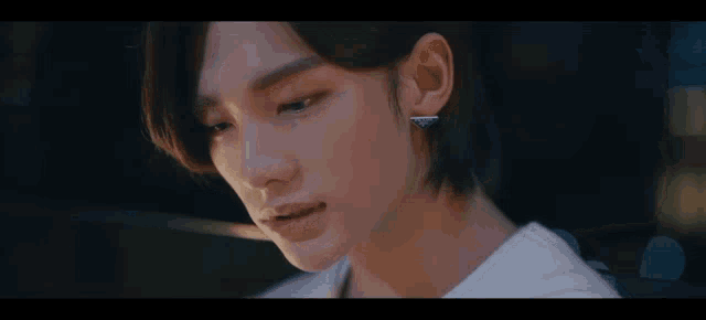 a close up of a young man 's face wearing earrings and a white shirt .