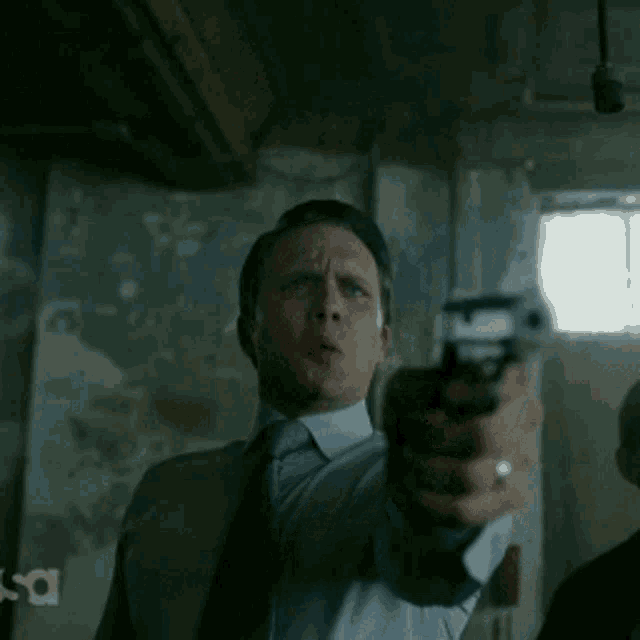 a man in a suit and tie is pointing a gun at the camera with the letters sa behind him