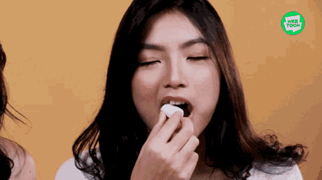a woman is eating a marshmallow with a web toon logo in the background