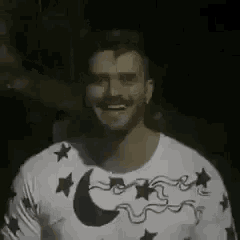 a man with a beard is wearing a white shirt with stars and a moon on it .