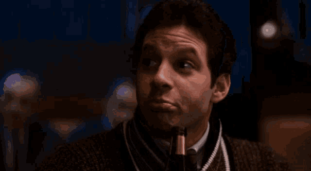 a man in a sweater and tie is looking at the camera with a surprised look on his face .