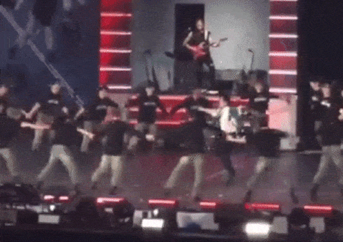 a group of people are dancing on a stage with a man playing a guitar