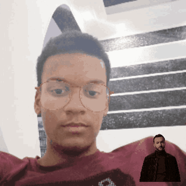 a man wearing glasses and a maroon shirt is looking at the camera