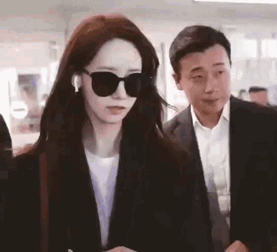 a woman wearing sunglasses is standing next to a man wearing a suit .