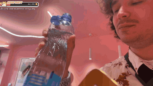 a man holding a bottle of water in front of a pink wall with a king kitty badge on it