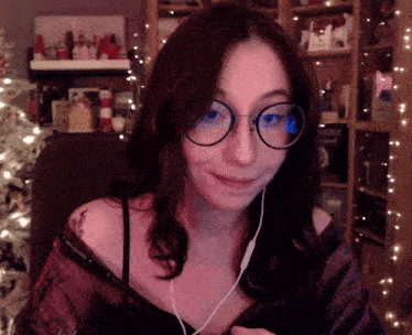 a woman wearing glasses and headphones is smiling in front of a christmas tree