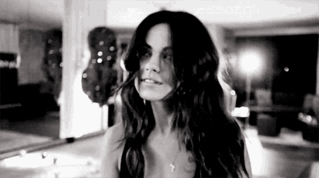 a woman with long hair is standing in front of a mirror in a room .