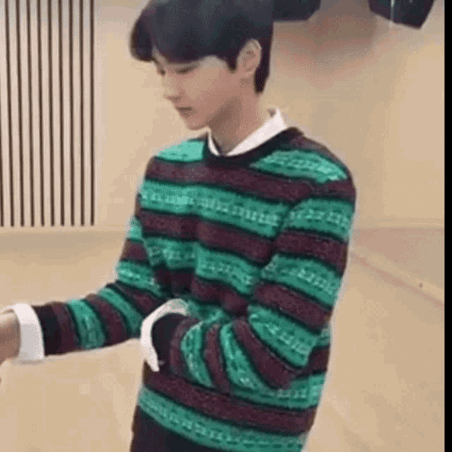 a young man wearing a green and red striped sweater is standing in front of a wall .