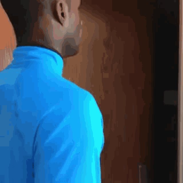 a man in a blue shirt is standing in front of a wooden door and looking at something .