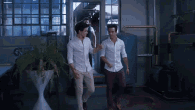 two men in white shirts are standing next to each other in a room holding hands