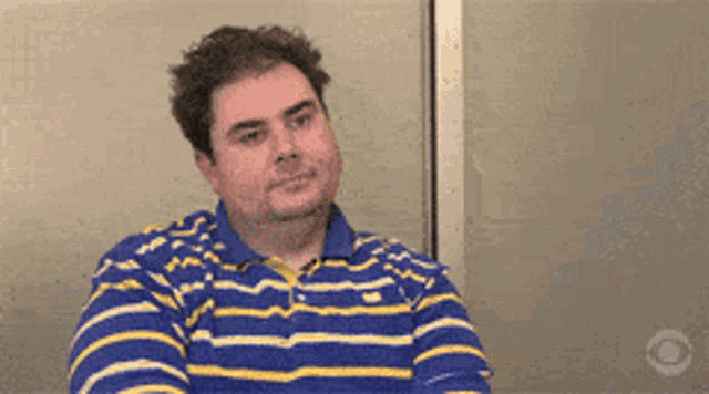 a man in a blue and yellow striped shirt is sitting in front of a window