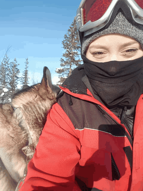 a woman wearing ski goggles and a red jacket holds a dog