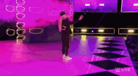a man is standing on a stage with a purple background and a purple light behind him .