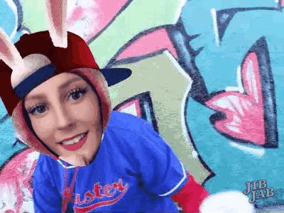 a woman wearing a bunny hat and a jersey that says easter is standing in front of a graffiti wall .