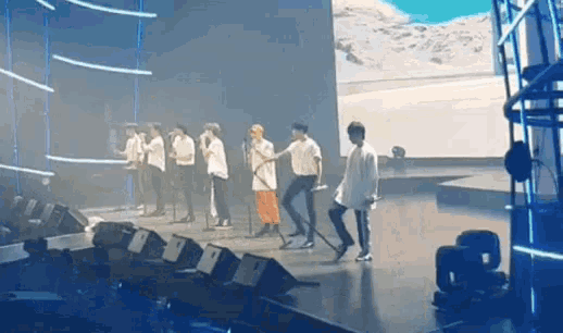a group of people are standing on a stage singing into microphones