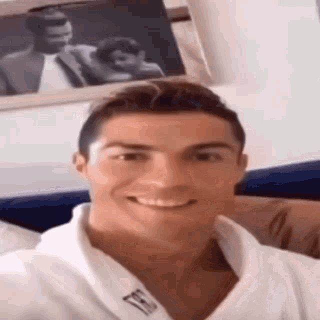 a man in a white robe is smiling and taking a selfie in front of a framed picture .