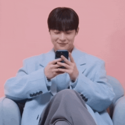 a man in a light blue coat is sitting in a chair looking at his phone