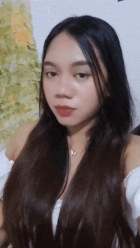 a woman with long black hair is wearing a white off the shoulder top and a butterfly necklace