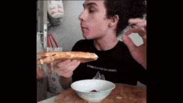 a man eating a slice of pizza next to a bowl with ketchup