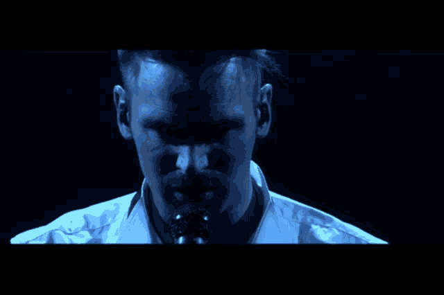 a man in a white shirt is singing into a microphone in a dark room