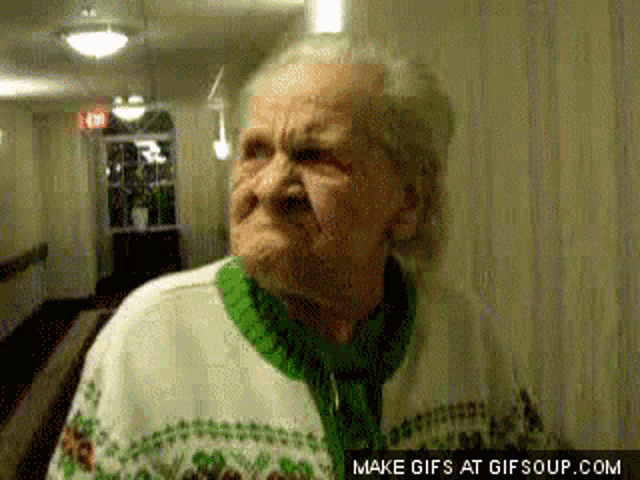 an elderly woman in a green and white sweater is making a funny face .