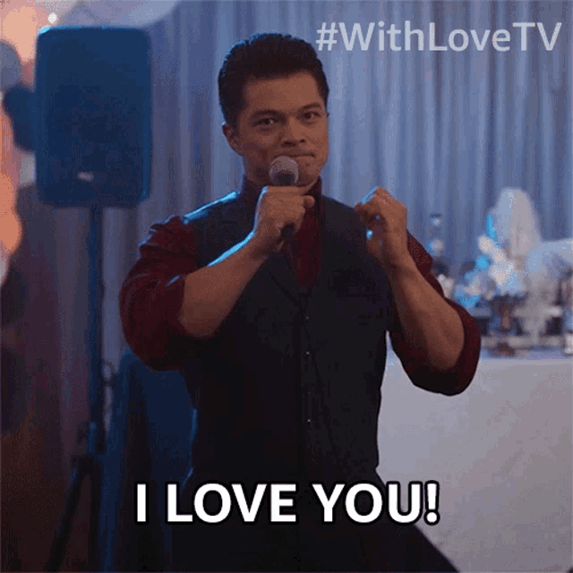 a man singing into a microphone with the words i love you behind him
