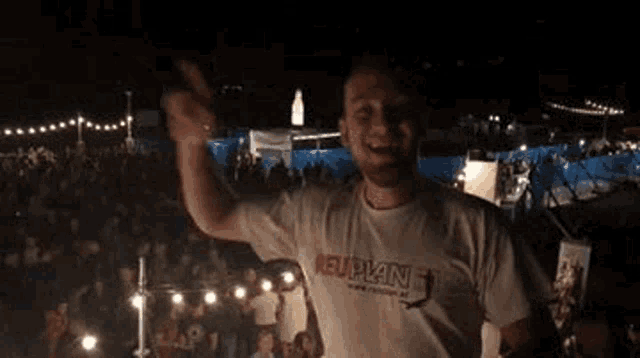 a man in a white t-shirt is standing in front of a crowd of people at a concert .