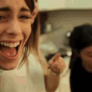 a woman is laughing with her mouth open and a man is behind her .