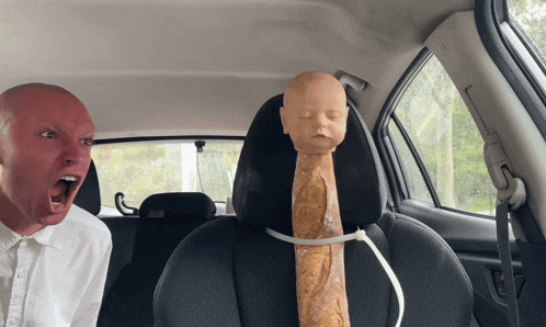 a man is sitting in a car with a mannequin head and a loaf of bread