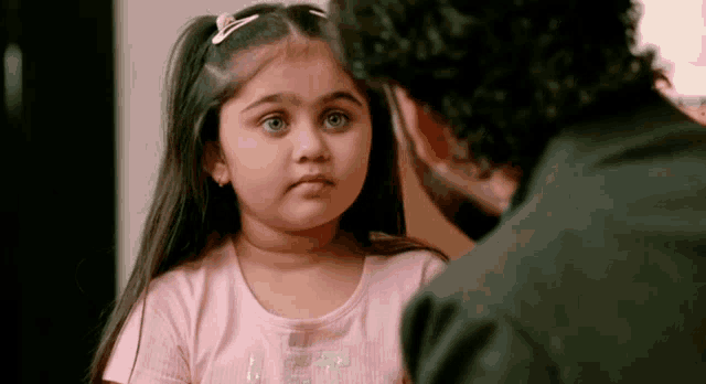 a little girl in a pink shirt is looking at a man .