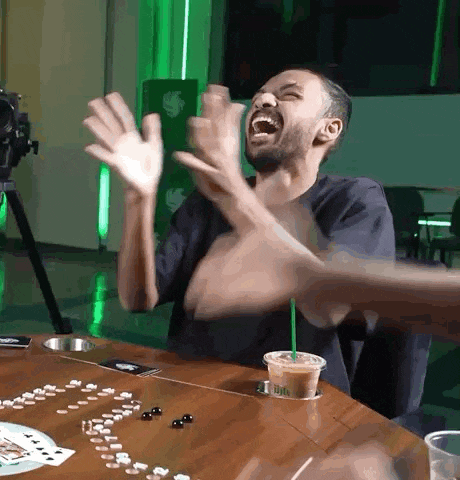 a man is sitting at a table with his hands in the air and a starbucks drink in his hand .